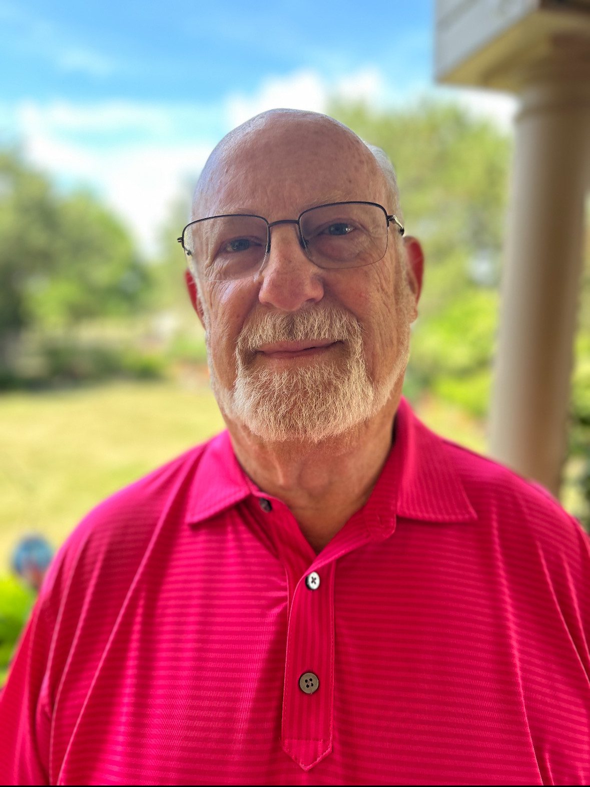 Smiling elderly man in a red shirt outdoors.