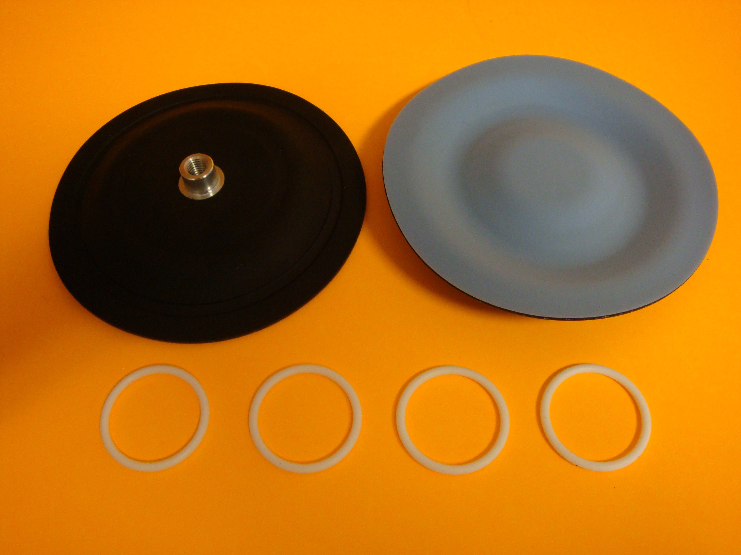 Two diaphragm components with five small rings on an orange surface.